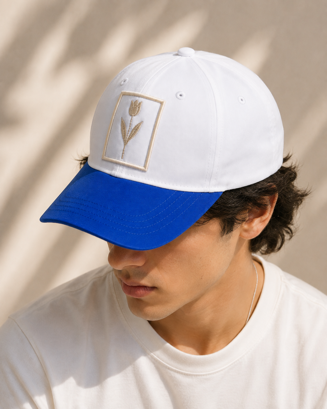 White and blue embroidered baseball cap with floral patch worn by a model